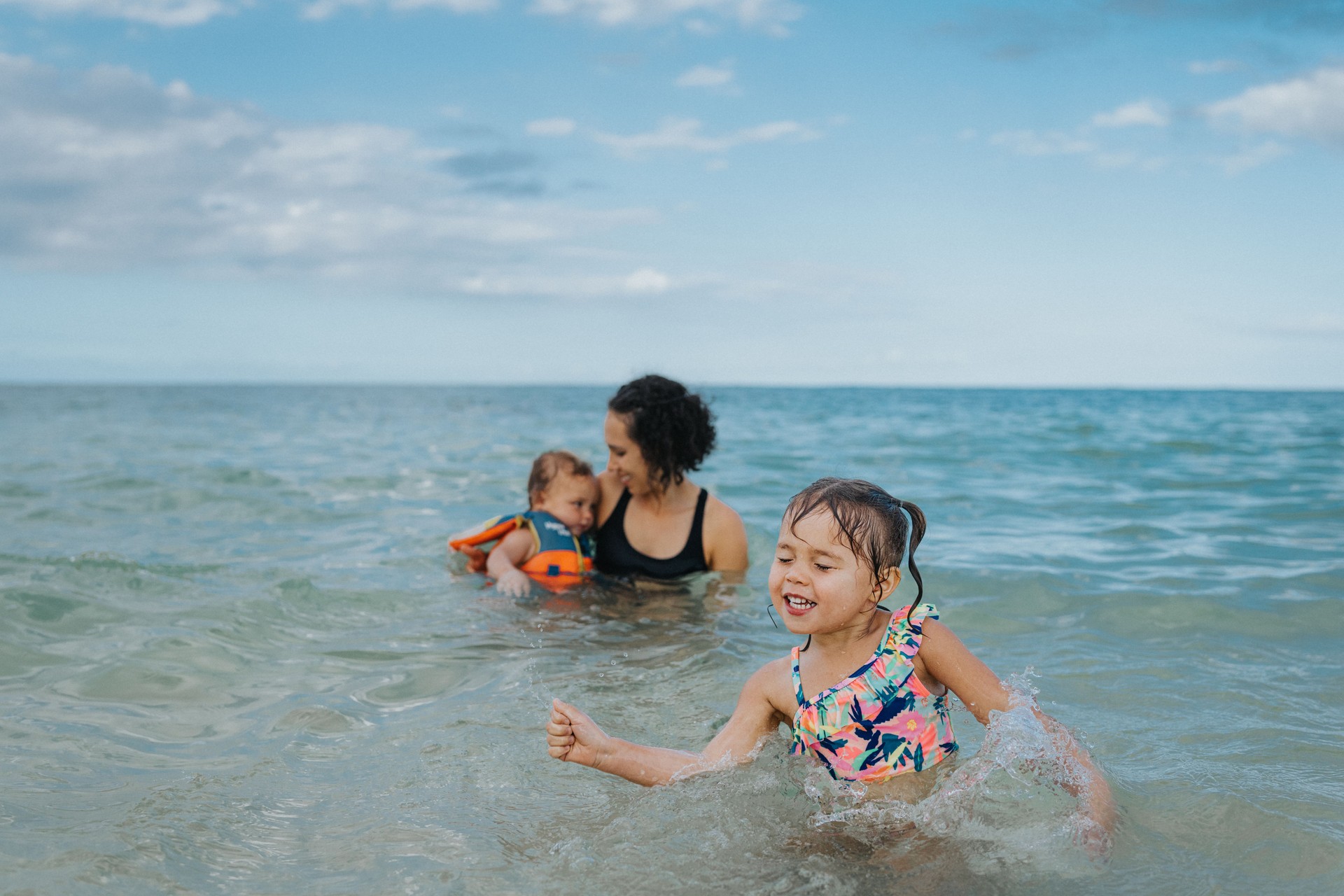 Happy little girl swimming with her mom and baby brother