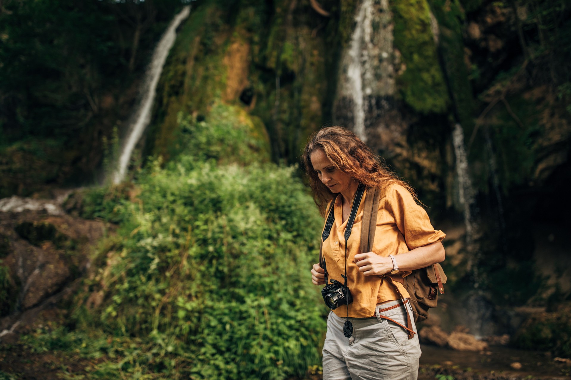 Lady explorer with camera standing by the waterfall